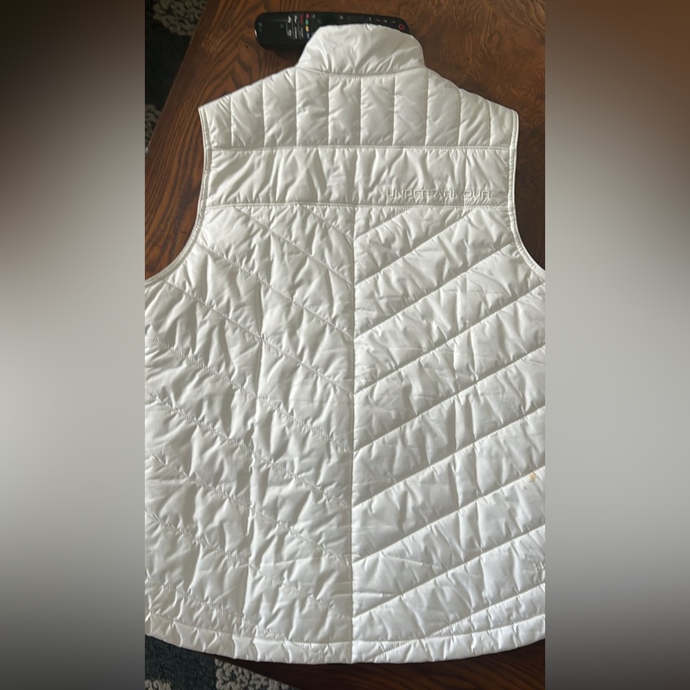 White UA Storm vest white w/ 3 zip pockets, one upper chest exterior pocket.